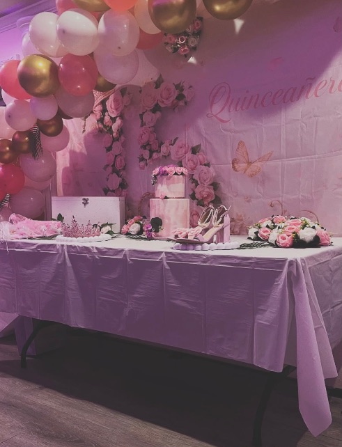 Quinceañera cake table with pink roses and a balloon garland