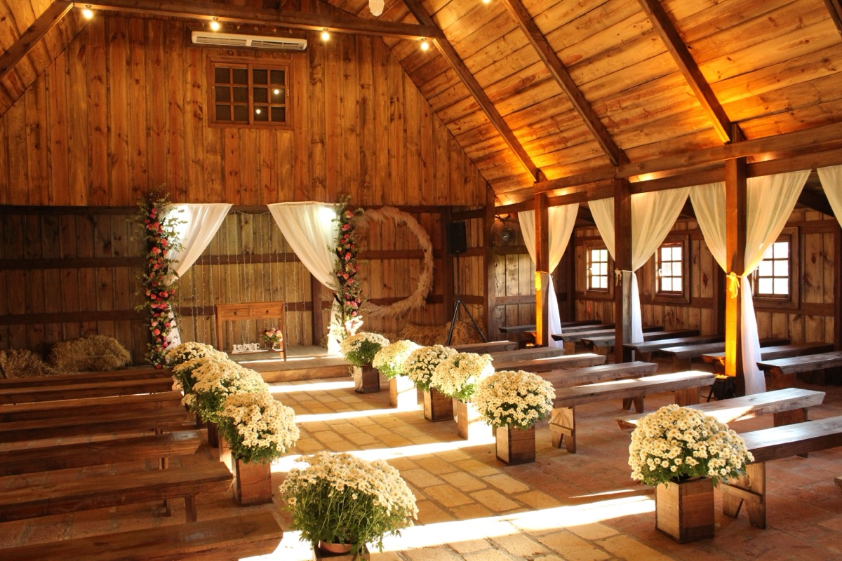 Rustic barn set for a wedding ceremony, with wooden benches and white daisies lining the aisle
