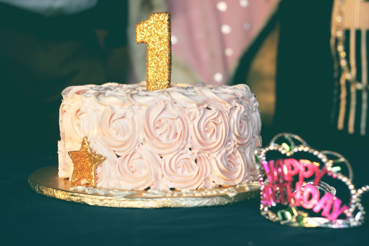 First birthday cake with pink rosette frosting, a glittering gold 1 topper and a Happy Birthday tiara